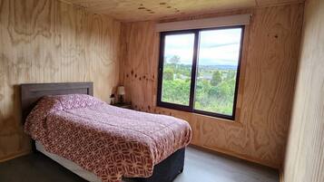 Ein Schlafzimmer mit Bett, Fenster und Holzwänden.