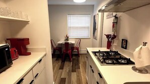 A modern kitchen with white cabinets, a red chair, a dining table, and a window with blinds.