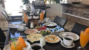 Ein Essbereich im Freien mit einem Tisch, der für ein Frühstück gedeckt ist, darunter Eier, Toast und Obst, zusammen mit Tassen Kaffee und Orangensaft.
