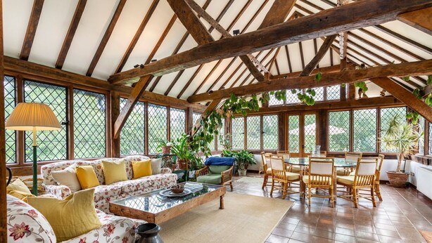 Une pièce spacieuse avec un plafond haut, des poutres apparentes, un ensemble de canapés, une table à manger avec des chaises et des plantes en pot.