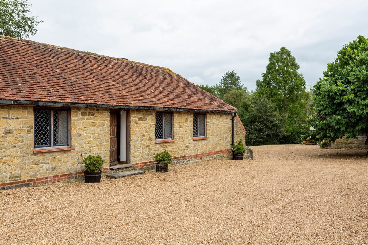 A stone building with a tiled roof, a gravel driveway, and potted plants.