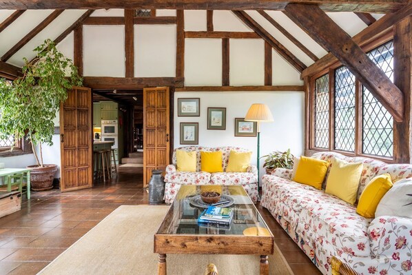 Una sala rústica con vigas de madera a la vista, un sofá floral y una mesa de centro de vidrio.