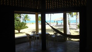 A beach view from a covered patio with a hammock, chairs, and a table. - Ponta Village - Paradise in Maragogi - Cottage 02 (Maragogi)