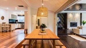 A modern kitchen with white cabinets, a wooden dining table, and a hanging light fixture. - Pet Friendly - Bellini Bliss with Gas Heated Pool (Tootgarook)