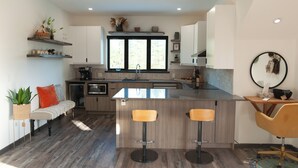 A modern kitchen with a central island, bar stools, and a seating area with a bench and a plant. - The Truffle Hut Parksville (Parksville)