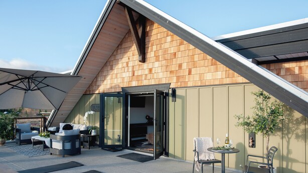 A modern outdoor patio area with a wooden sloped roof, a glass door entrance, outdoor seating, and a small table with a potted plant. - The Truffle Hut Parksville (Parksville)