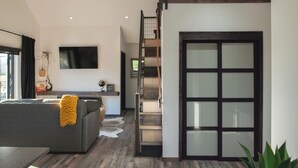 A modern living room with a grey sofa, a flat-screen TV, and a staircase leading to an upper level. - The Truffle Hut Parksville (Parksville)