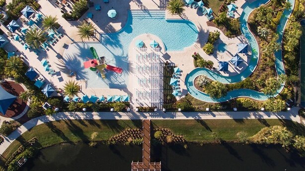 An aerial view of a resort with a central swimming pool, a water slide, and a dock extending into a lake. - Entire Home in Kissimmee, FL - Windsor at Westside (Kissimmee)