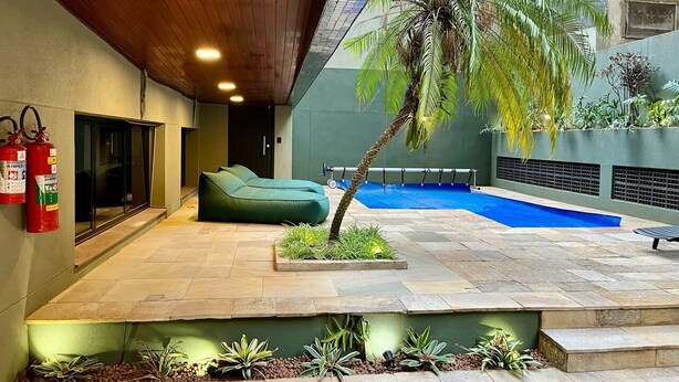 A modern outdoor area with a pool, a green sofa, and a palm tree.