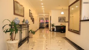 A hotel corridor with marble flooring, potted plants, framed artwork, and a reception desk.