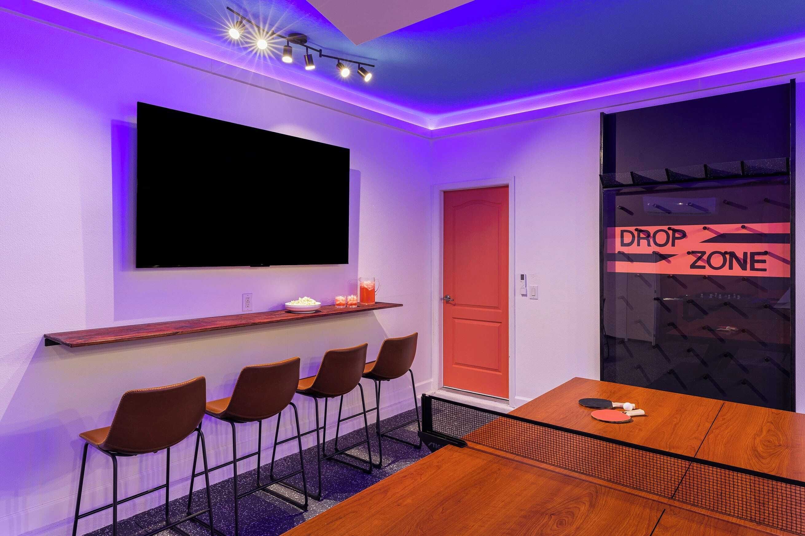 A conference room with a large flat-screen TV, a wooden table, four chairs, and a 'DROP ZONE' sign on the glass door.