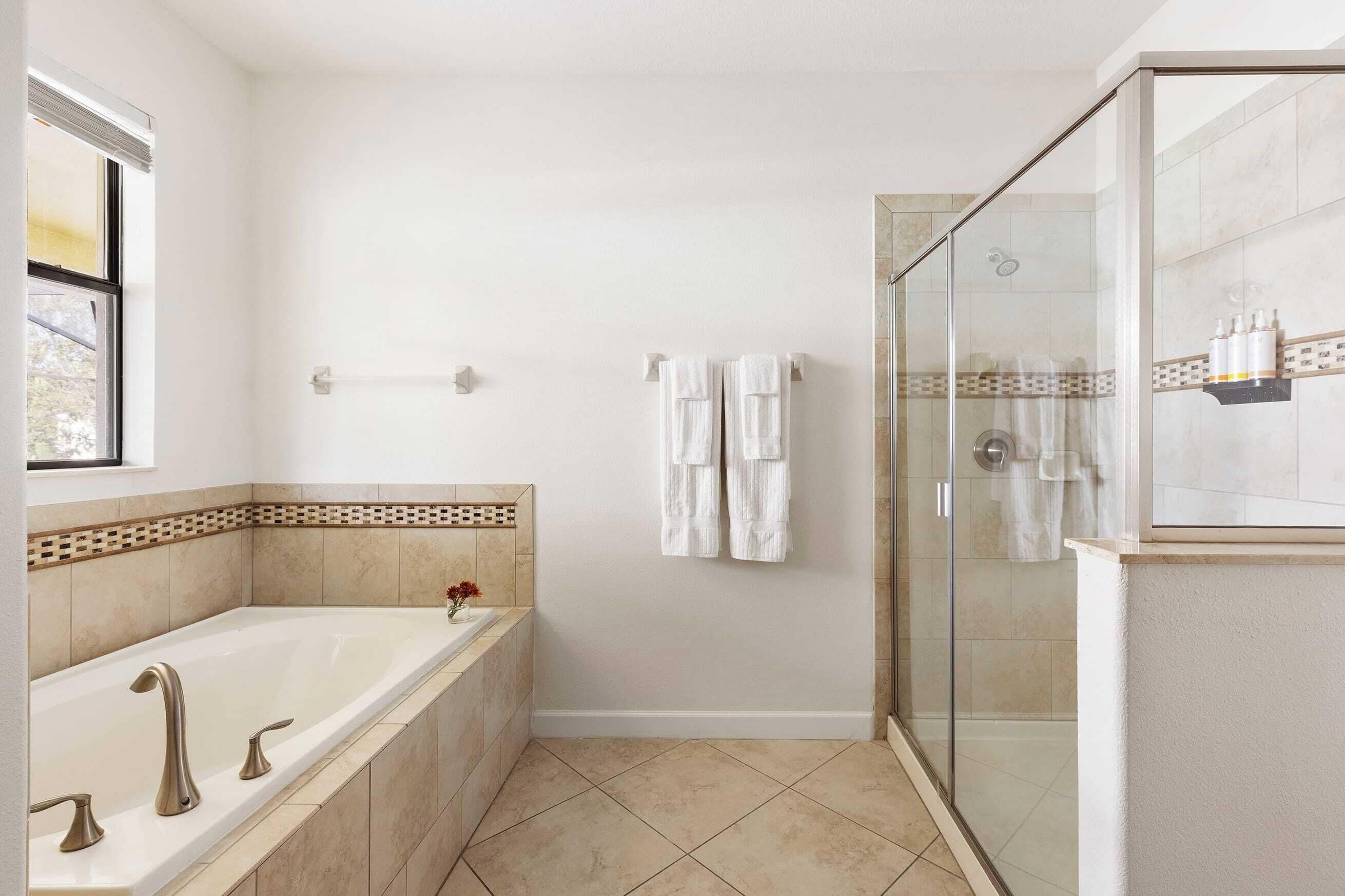 A modern bathroom with a bathtub, a glass-enclosed shower, and a window.
