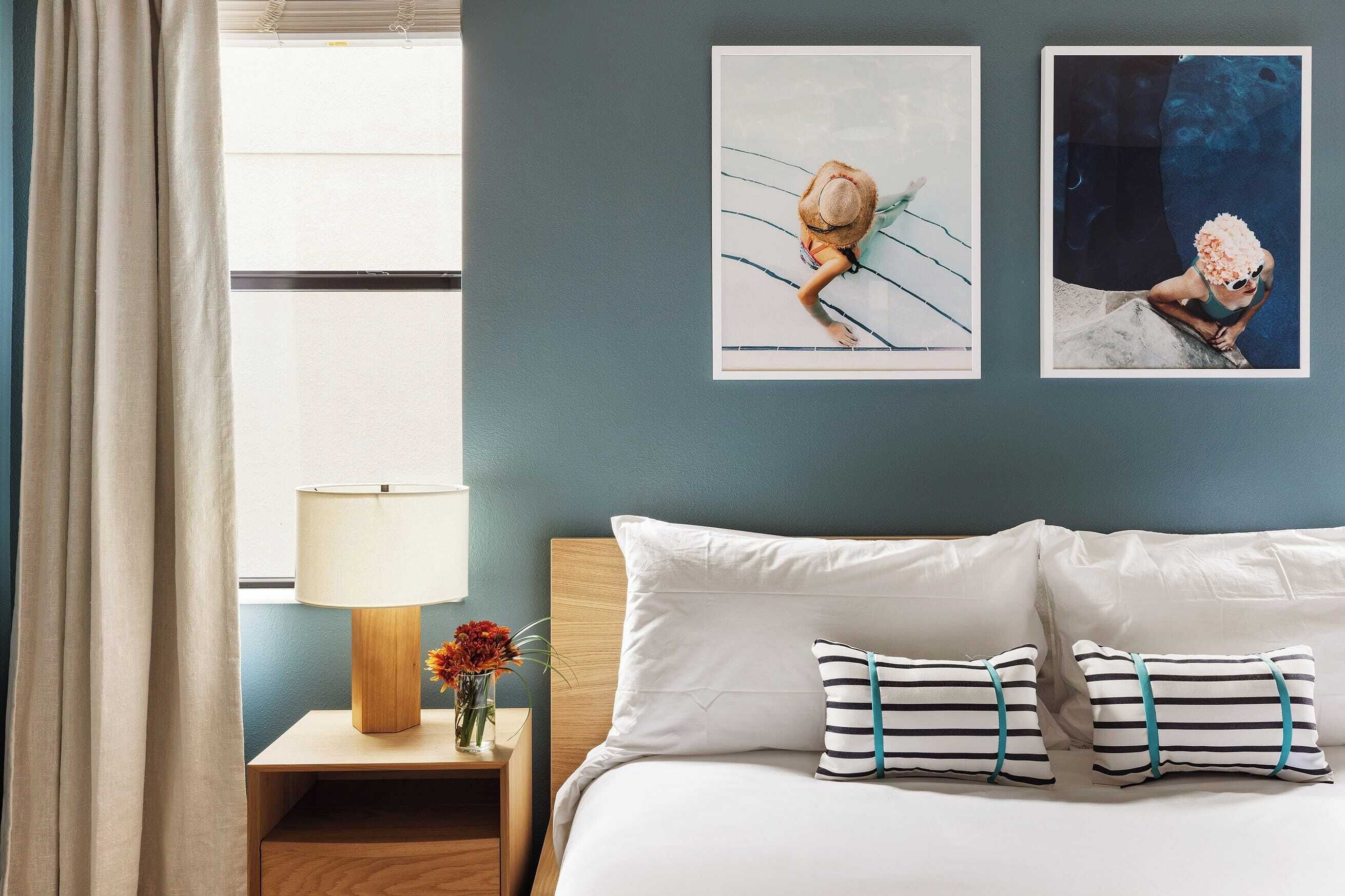 Una camera d'albergo con un letto, un comodino con una lampada e due quadri appesi al muro.