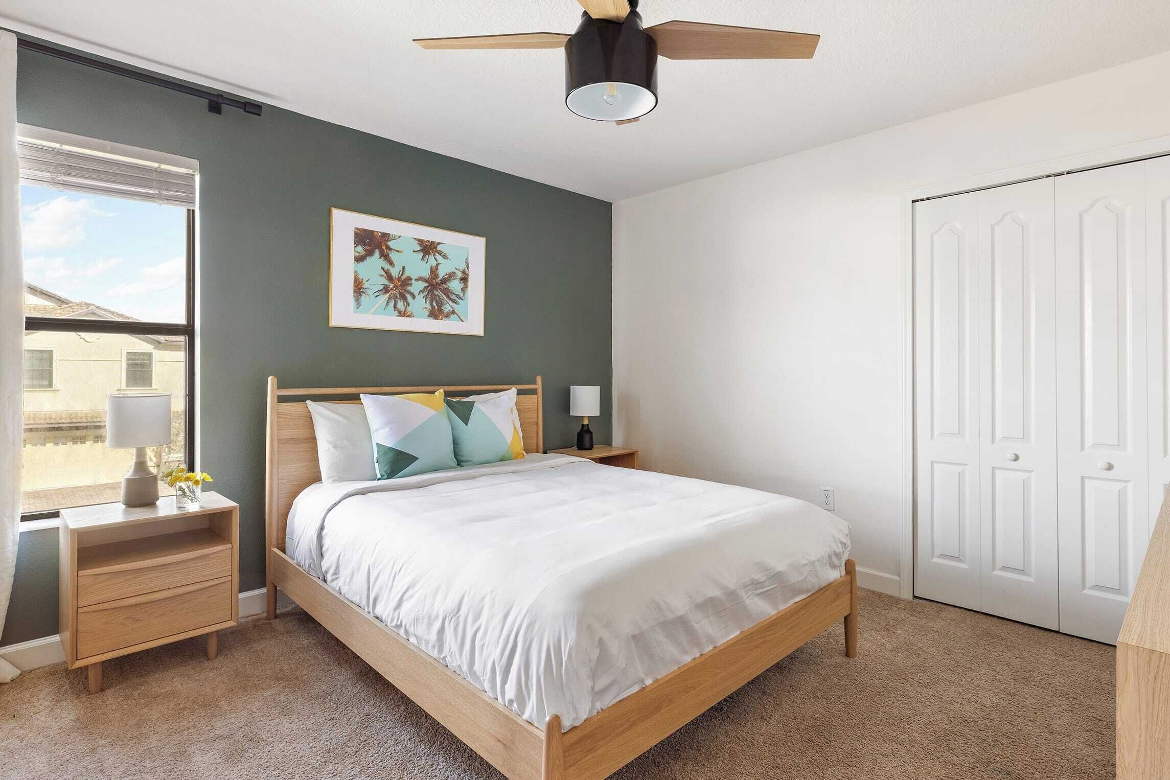 Une chambre à coucher avec un lit, des tables de chevet, un ventilateur de plafond, une fenêtre et une porte.