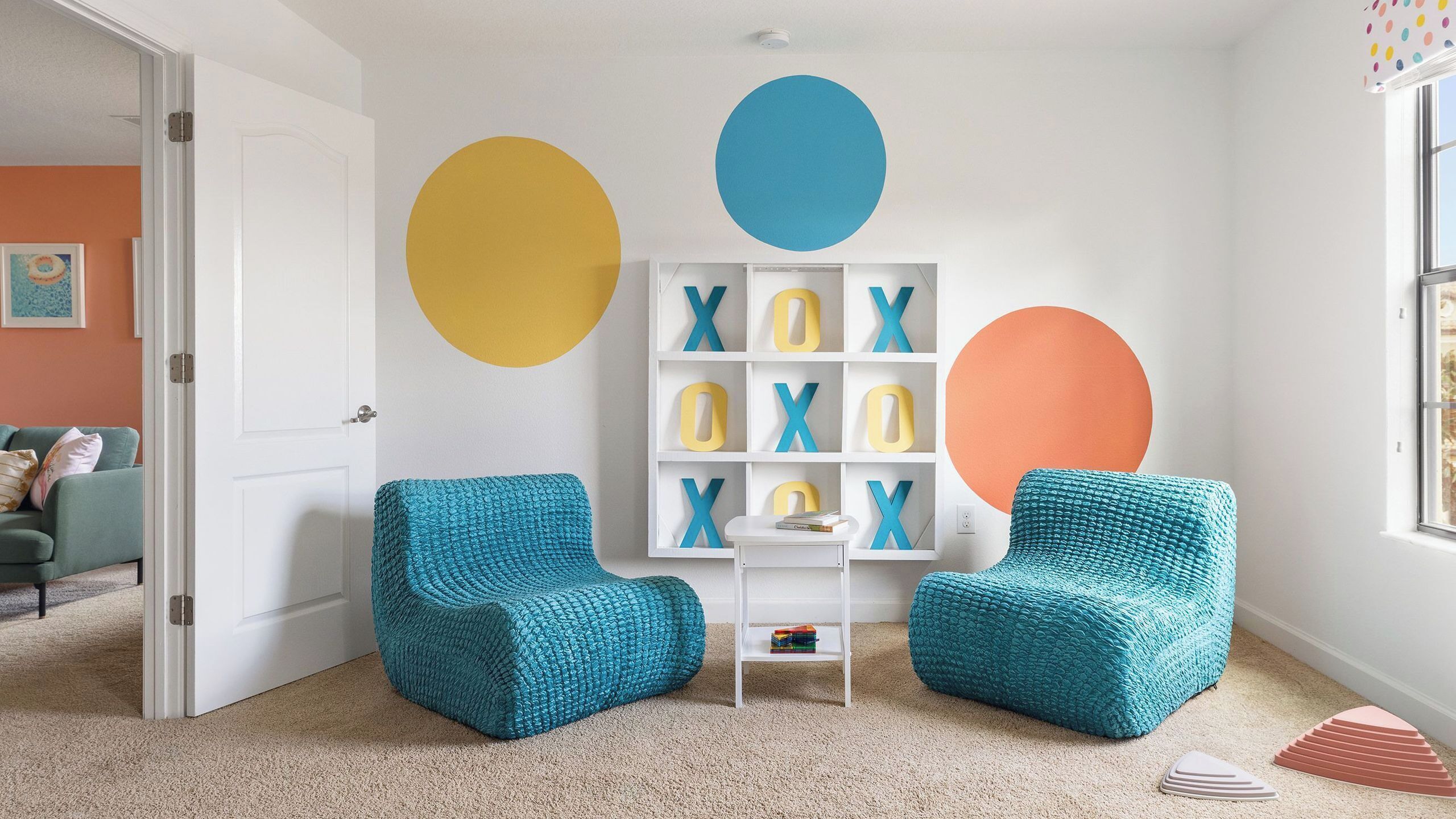 Una habitación con sillones de felpa color turquesa, una estantería blanca con letras del alfabeto y un ventanal grande.
