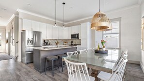 Een moderne keuken met witte kasten, roestvrijstalen apparatuur, een glazen kookeiland en een eethoek met witte stoelen.