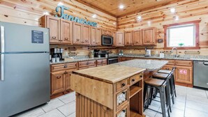 A kitchen with wooden cabinets, a granite countertop, a stainless steel refrigerator, a microwave, and a sink. - Laurel Point by Avantstay Sleeps 18! Indoor Pool, Hot Tub, Theater, Game Room (Sevierville)
