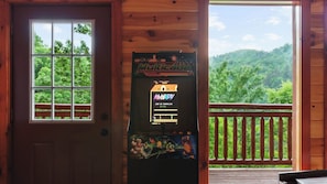 Eine Holzhütte mit Spielgerät, einem Fenster mit Blick auf Bäume und einer Holzterrasse.