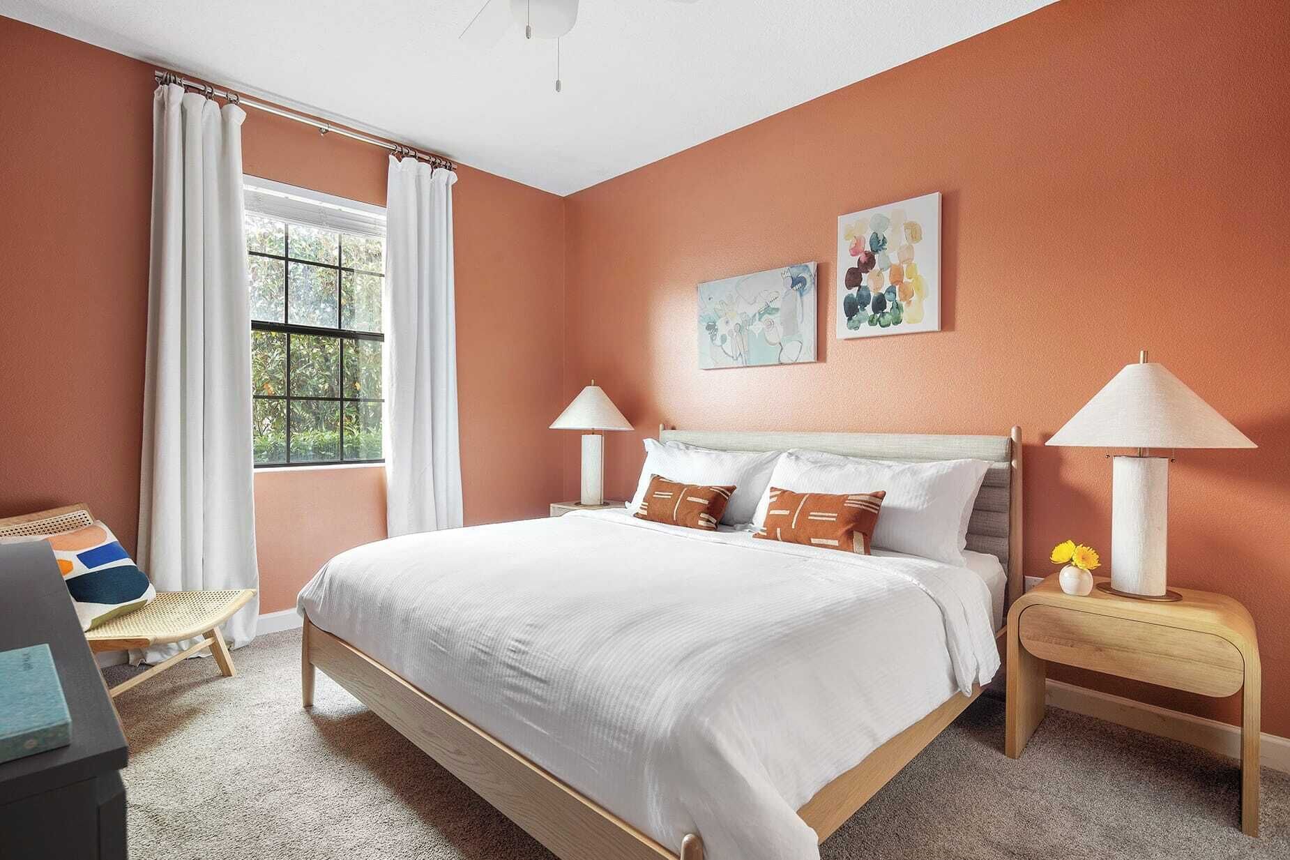 A bedroom with a bed, two bedside tables, a window with curtains, and artwork on the wall.