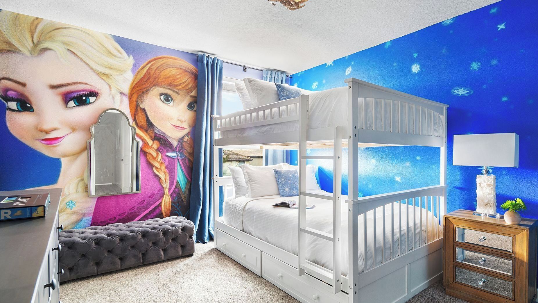 Un lit superposé avec une structure blanche, une table de chevet avec une lampe et une fresque murale.