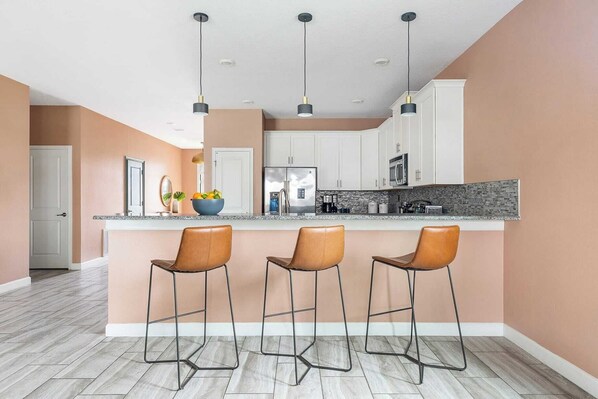 A modern kitchen with three bar stools, a central island, and pendant lighting. - Sleeps 16! 8bdr Kid Haven w/ Pool & Arcade Orlando Resort Retreat by Avantstay (Davenport)