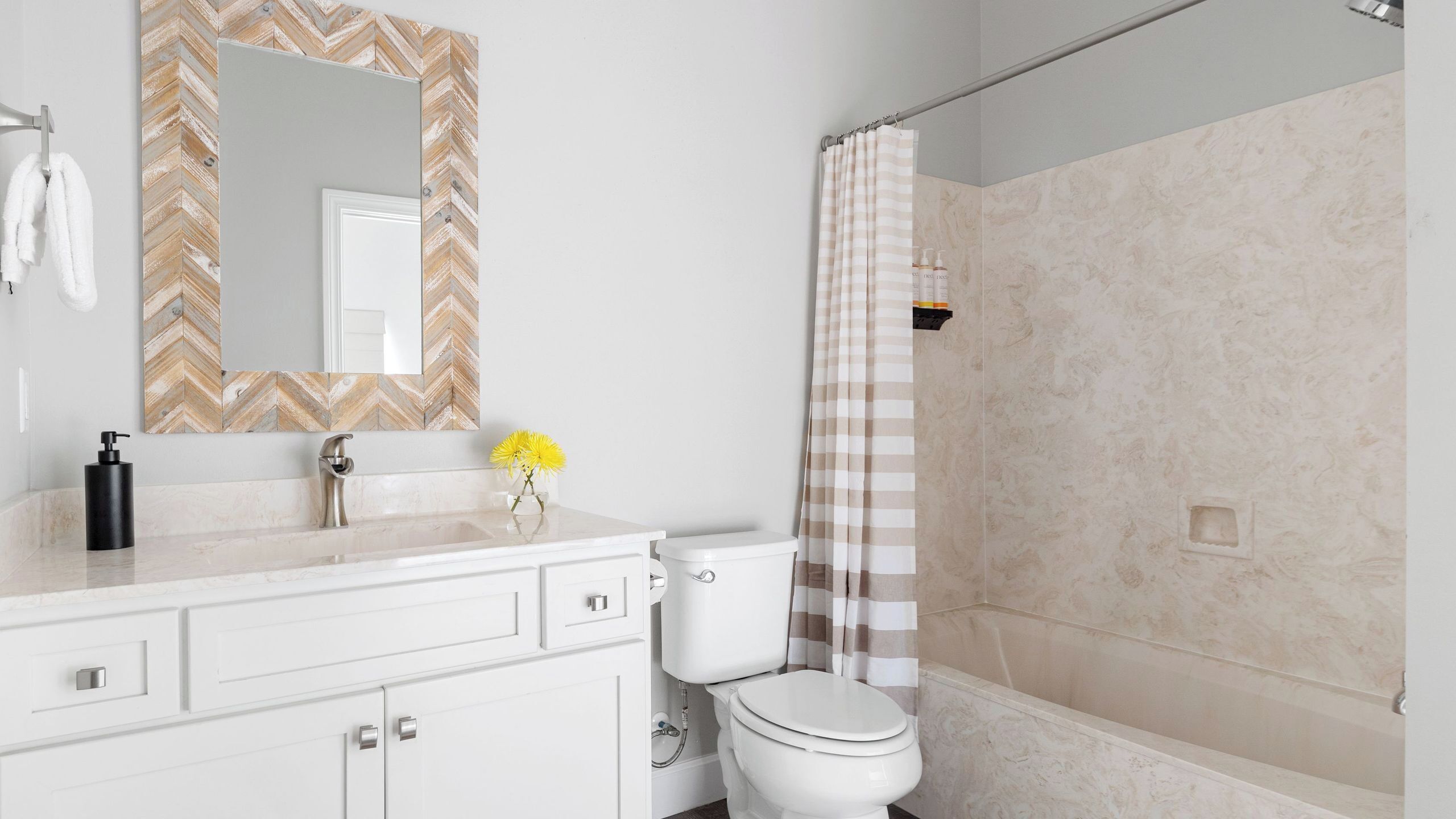 A bathroom with a white vanity, a mirror with a chevron pattern, a toilet, and a shower with a checkered curtain.
