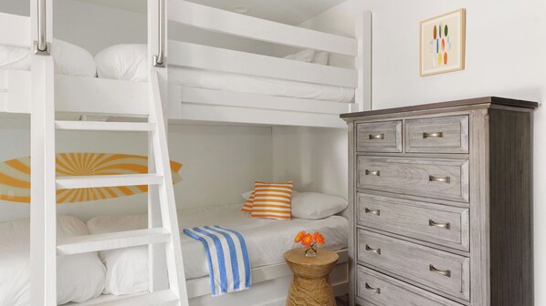 A bunk bed with white bedding, a striped pillow, and a blue-striped towel. There is a wooden dresser with drawers and a small round table with a vase of flowers. - Villa Near Beach w/ Pool & Outdoor Dining Bohemian Beach Retreat by Avantstay (Destin)