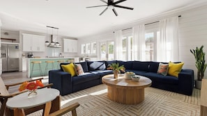 A spacious living room with a dark blue sofa, a round wooden coffee table, and a kitchen in the background.