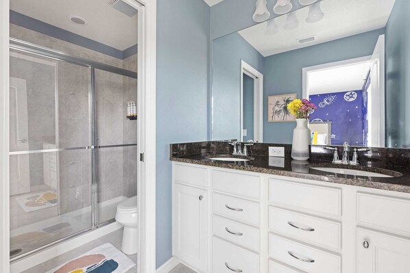 Un baño con cabina de ducha de vidrio, inodoro blanco, tocador doble con espejo y una pared de acento azul.