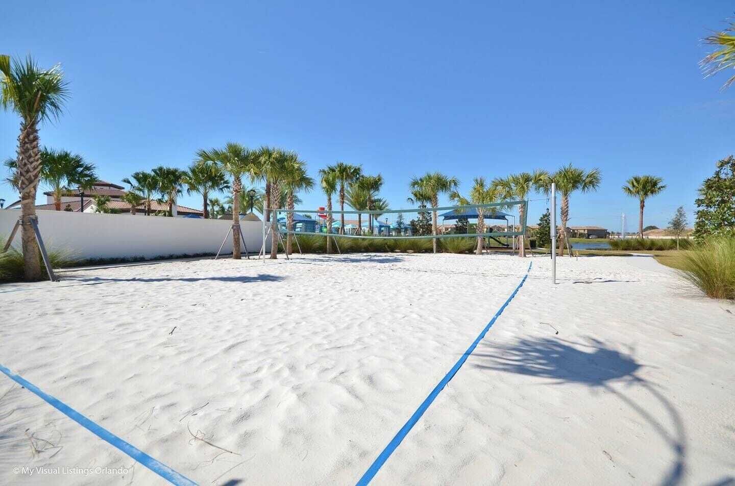 A beach volleyball court with a net, surrounded by palm trees and a clear sky.