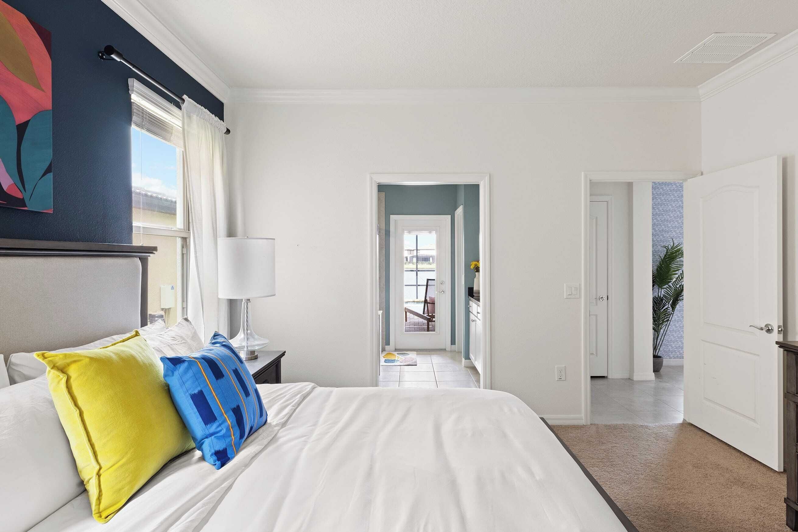 Une chambre d’hôtel avec un lit, une table de chevet, une lampe, une fenêtre avec des rideaux, une porte et une vue sur l’extérieur.