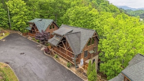 Un bâtiment de style « cabane en rondins », avec des fondations en pierre, entouré d’une végétation luxuriante et doté d’une allée pavée.