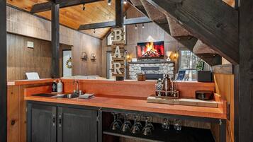 A rustic interior with a wooden bar area, a stone fireplace, and a kitchen counter.