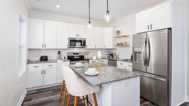A modern kitchen with white cabinets, stainless steel appliances, a granite countertop, and a bar stool.