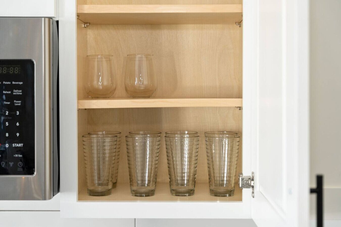 A kitchen cabinet with a built-in microwave and a shelf with four clear glass tumblers.