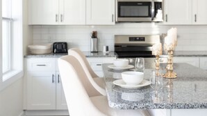 A modern kitchen with white cabinets, a stainless steel microwave, a coffee maker, and a marble countertop.