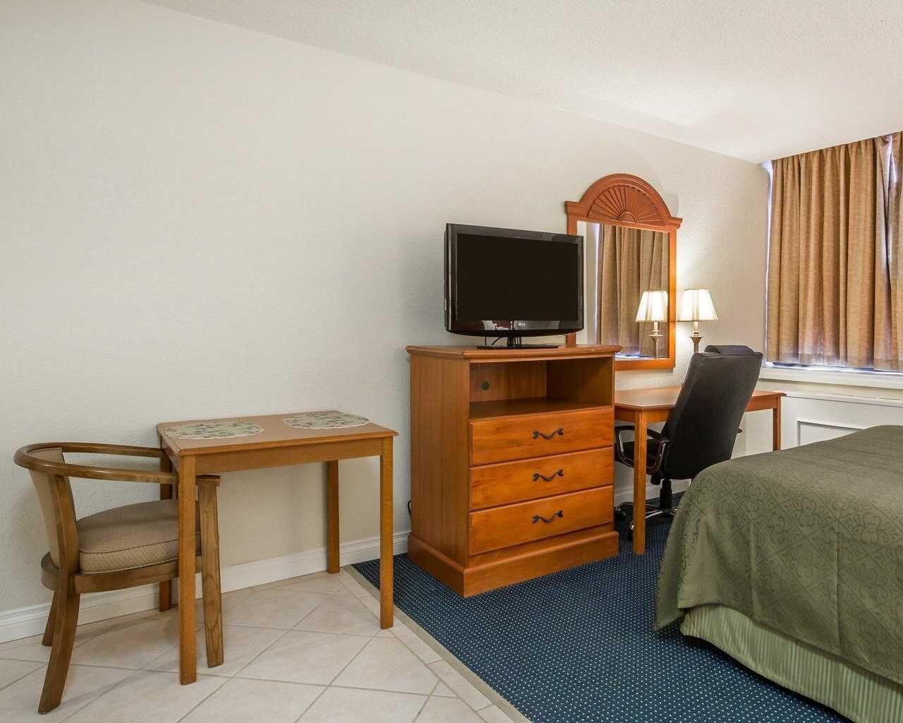 Habitación de hotel con cama, escritorio con televisor, silla, cómoda y ventana con cortinas.