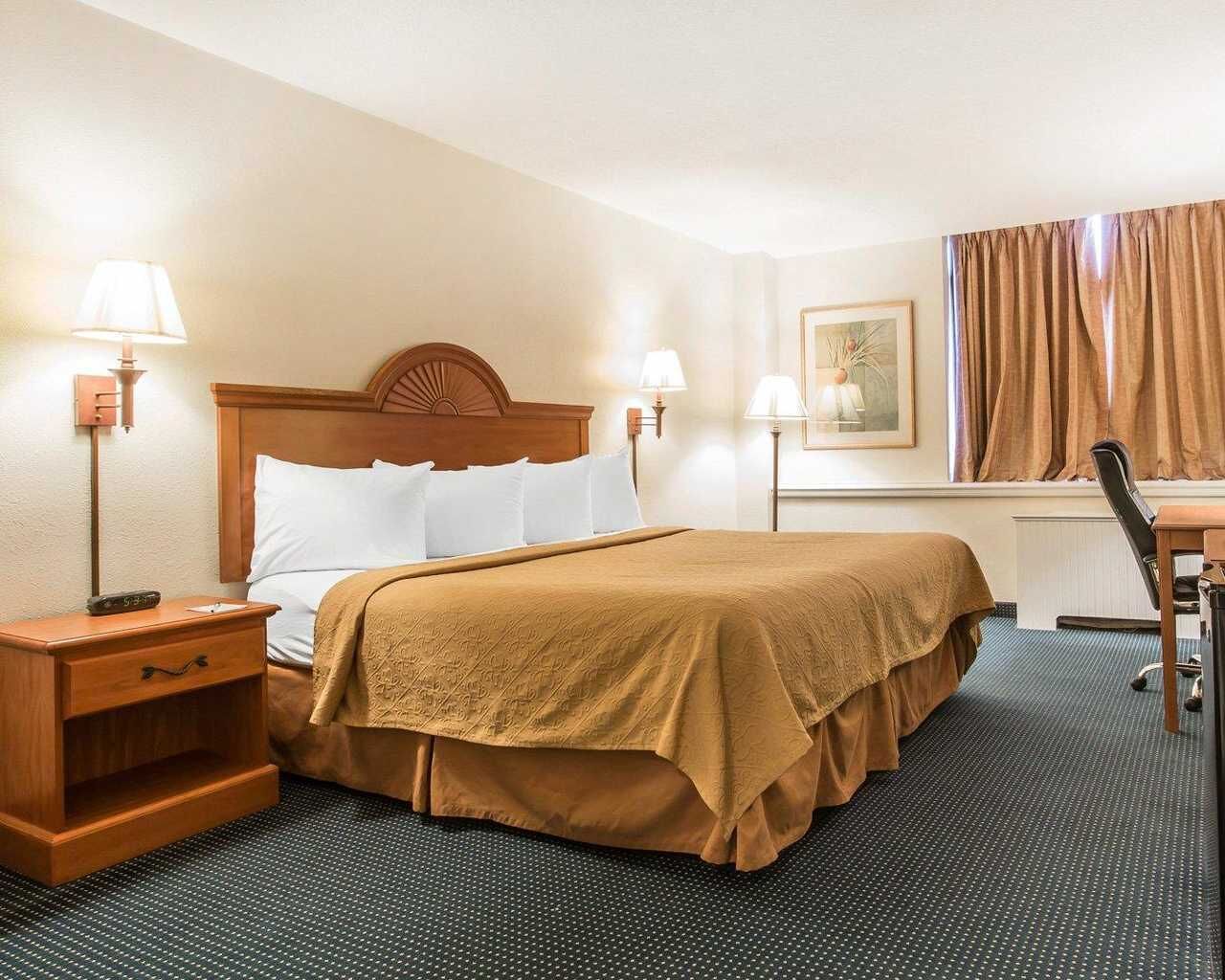Una habitación de hotel con cama, mesitas de noche, lámparas, un escritorio y una silla.