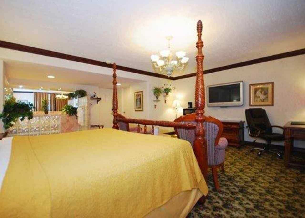 A hotel room with a four-poster bed, a desk with a chair, and a television on the wall.