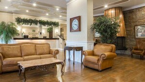 A lobby with a reception desk, leather sofas, a wooden coffee table, and a large clock on the wall. - St. Lawrence Hotel  (Massena)