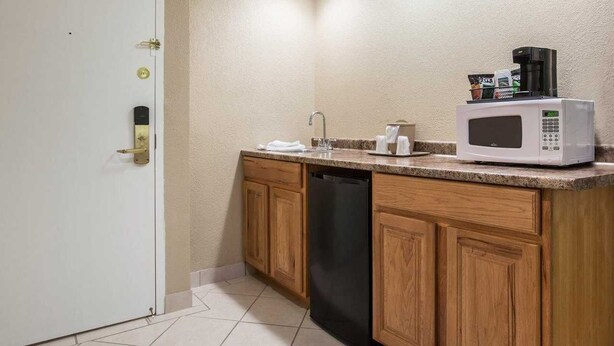 A compact kitchen with wooden cabinets, a black dishwasher, a white microwave, and a coffee maker on the countertop. - St. Lawrence Hotel  (Massena)