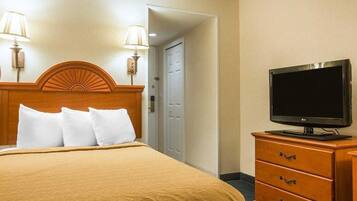 A hotel room with a bed, two wall-mounted lamps, a television on a dresser, and a door leading to another room.