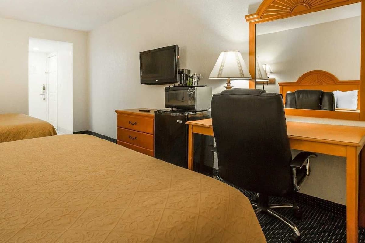 A hotel room with two beds, a desk with a computer and a lamp, a television, and a mirror.
