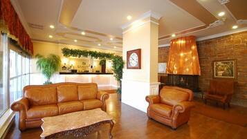 A lobby with leather sofas, a coffee table, a reception desk, a clock, a fireplace, and a stone wall.