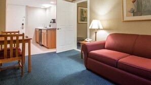 A hotel room with a dining area, a kitchenette, a red sofa, and a painting on the wall. - St. Lawrence Hotel  (Massena)