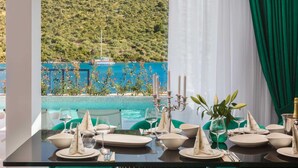A dining table set for six with a view of a pool and a boat in the background. - Beachfront Villa Seabird with Pool (Rogoznica)