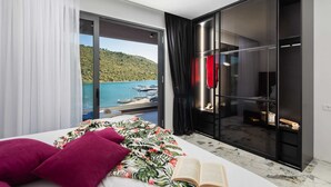 A modern bedroom with a large bed, a view of the sea, and a sliding glass door leading to a balcony. - Beachfront Villa Seabird with Pool (Rogoznica)