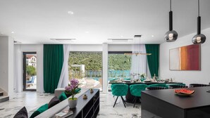 A modern living room with a dining area, large windows, and a view of a green landscape. - Beachfront Villa Seabird with Pool (Rogoznica)