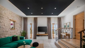 A modern living room with a green sofa, a coffee table, and a TV. There is a staircase with a railing leading to an upper level.
