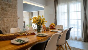 A dining area with a wooden table set for a meal, surrounded by chairs, with a vase of yellow flowers and a fruit bowl on the table.